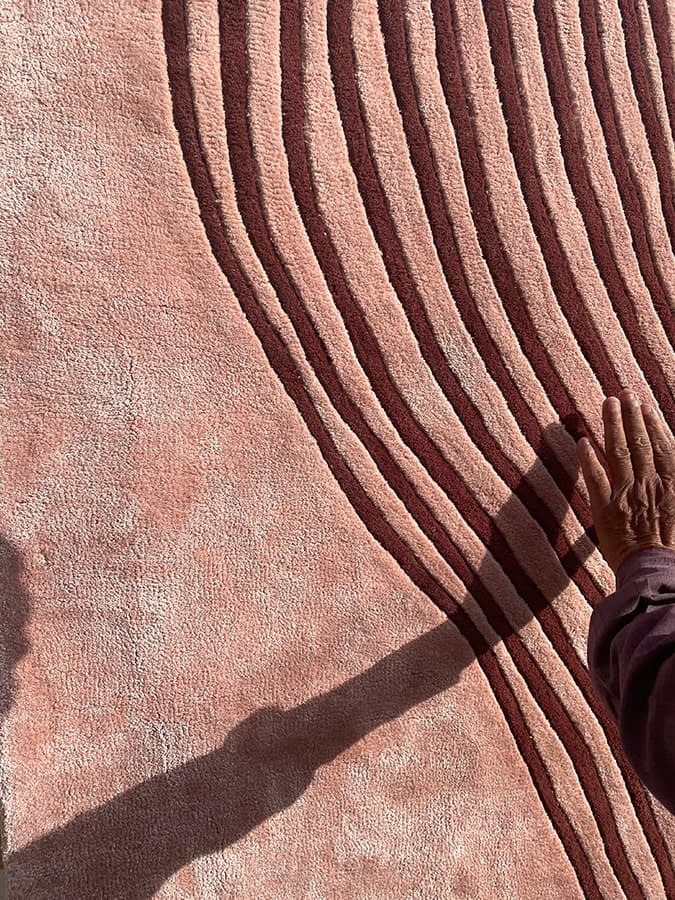 Textured pink rug with dark red curved lines and a hand touching the soft surface.