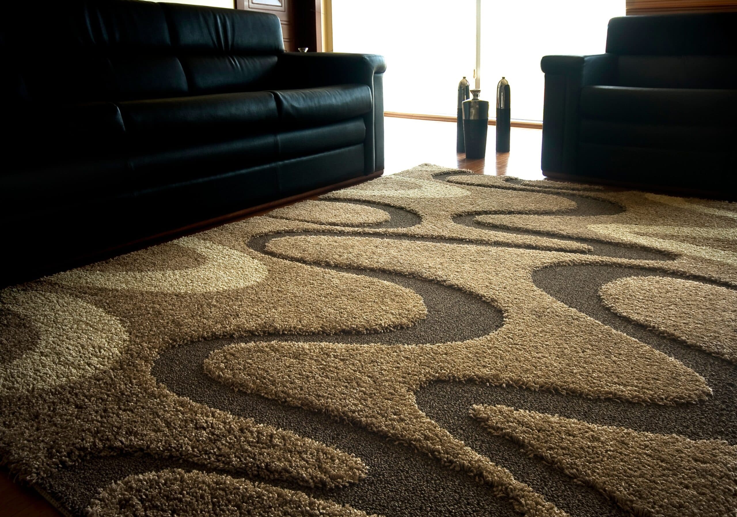 Textured brown and beige wavy patterned rug between a black leather sofa and armchair.