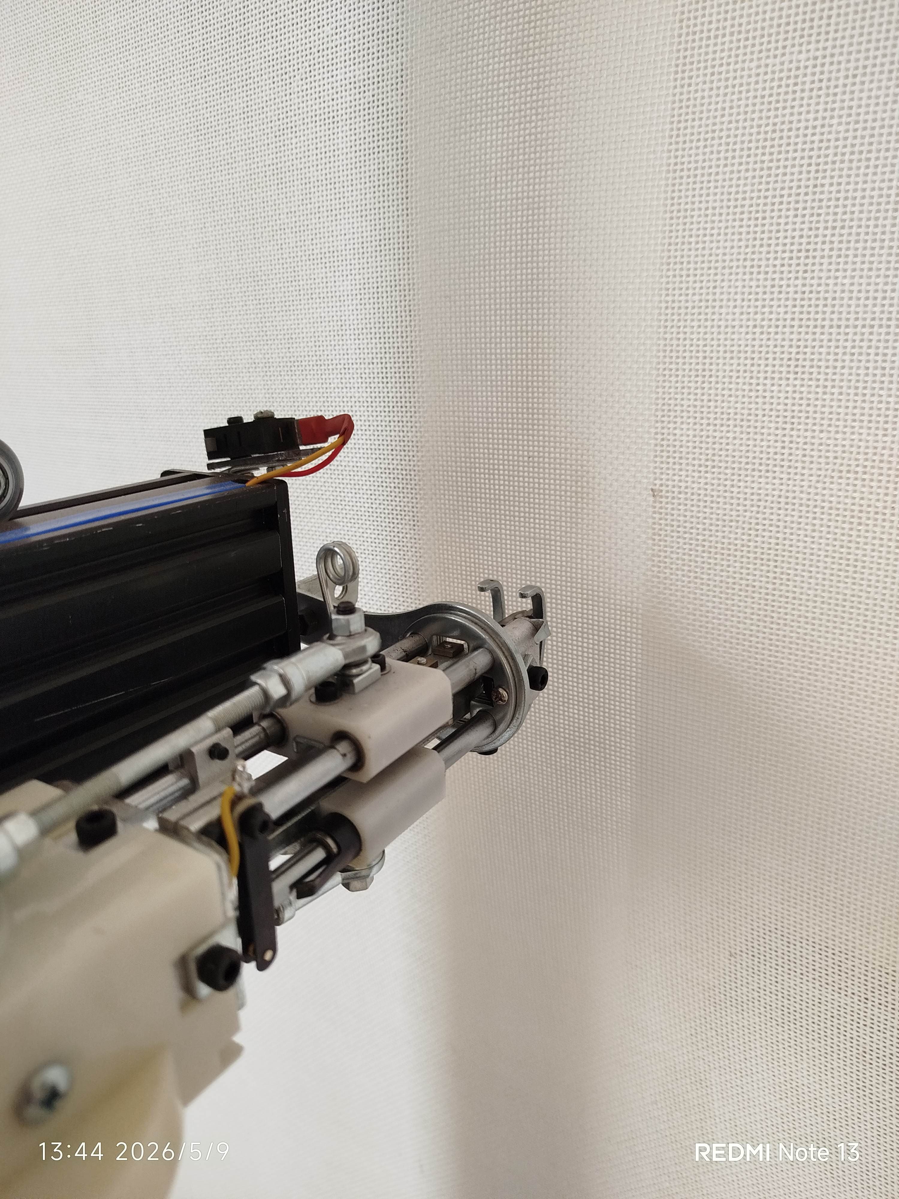 Close-up of a mechanical tufting gun mechanism against a white mesh fabric background.
