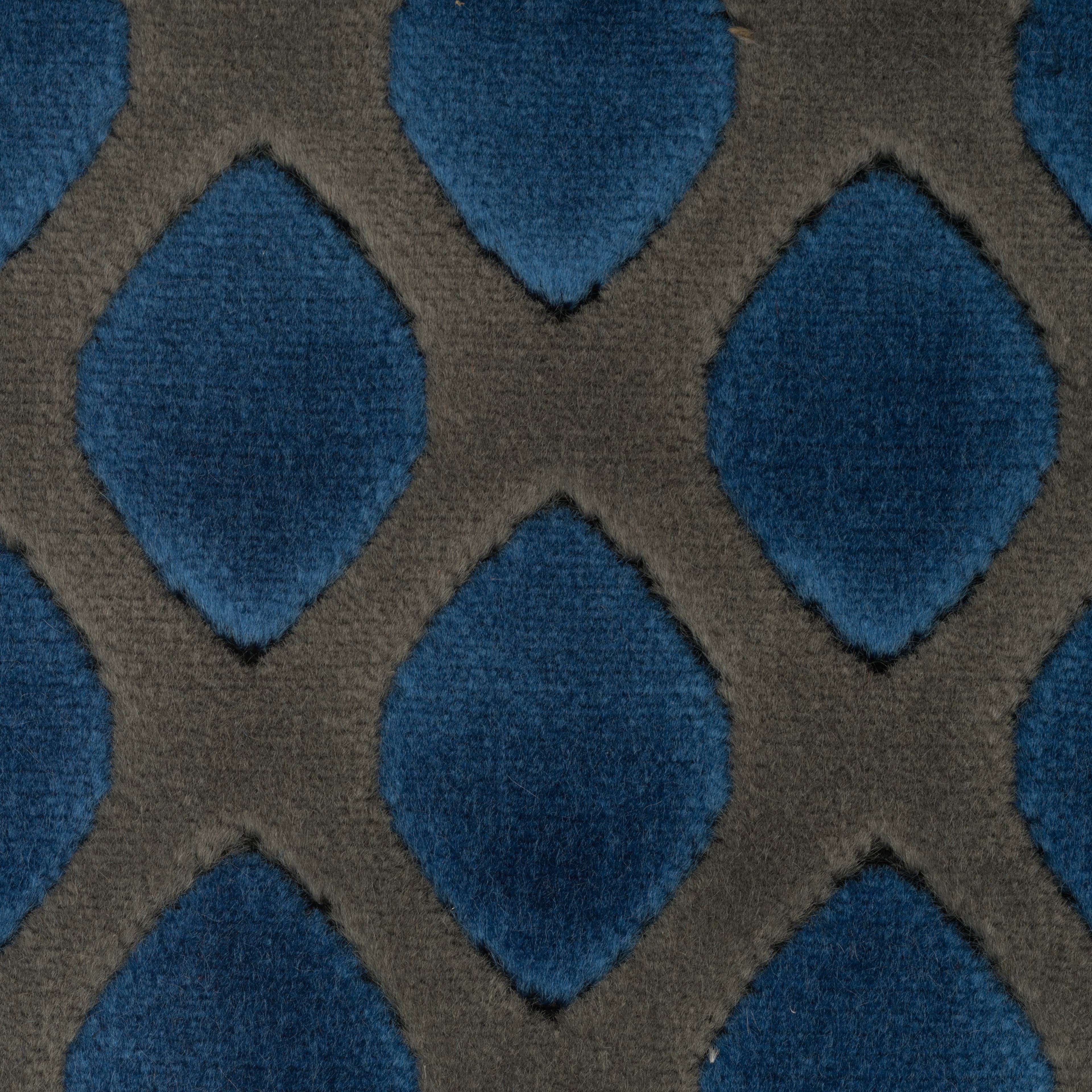 Textured blue velvet fabric featuring a repeating diamond pattern against a dark grey lattice background.